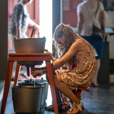 Kind zit op een melkkrukje in het museum de melkemmer te melken