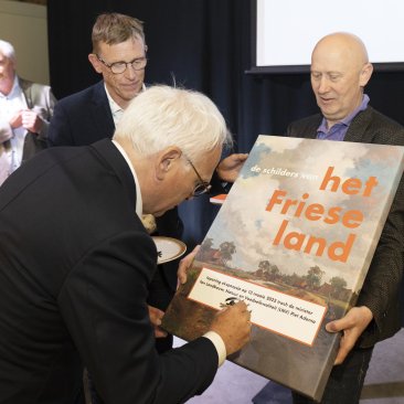 Minister Adema ondertekent de afbeelding van de expositie als openingshandeling, onder toeziend oog van voorzitter Kooistra, oud-directeur en expositiemaker Dijkstra en directeur Zandberg