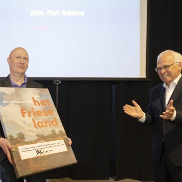 Directeur Zandberg presenteert het door minister Adema ondertekende afbeelding van de expositie.