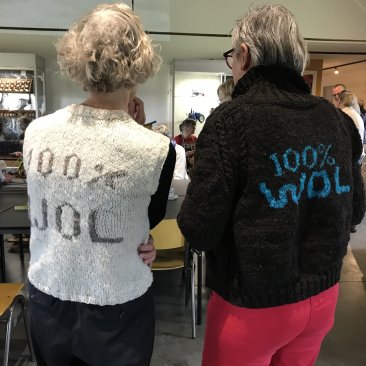 De achterkant van twee wolwerkers van Pleed met de tekst '100% Wol' op hun gebreide trui