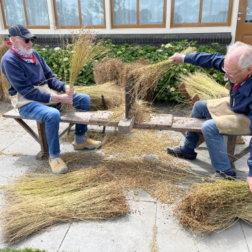 Twee personen repelen vlas op een repelbank voor het Fries Landbouwmuseum