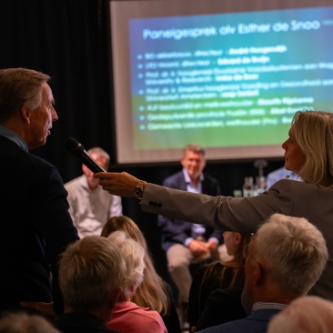 Een bezoeker uit het publiek stelt een vraag aan het panel tijdens een debat onder leiding van Esther de Snoo