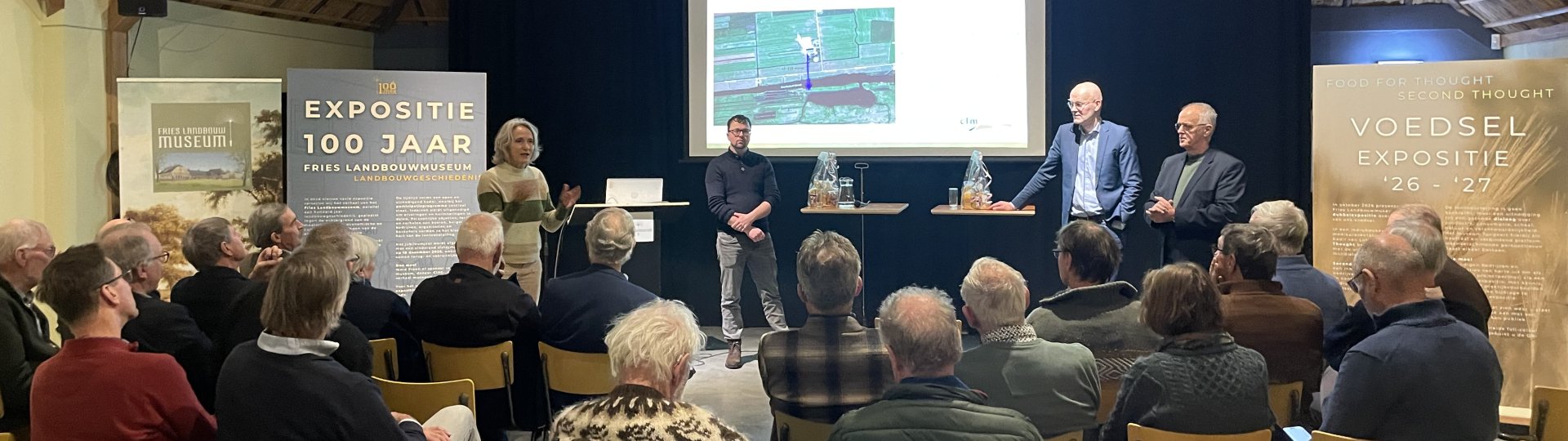 Debat "Niet alles kan overal, aldus Johan Remkes" in het Fries Landbouwmuseum. Voor het presentatiescherm staan sprekers leden van het Lânboukundich Wurkferbân