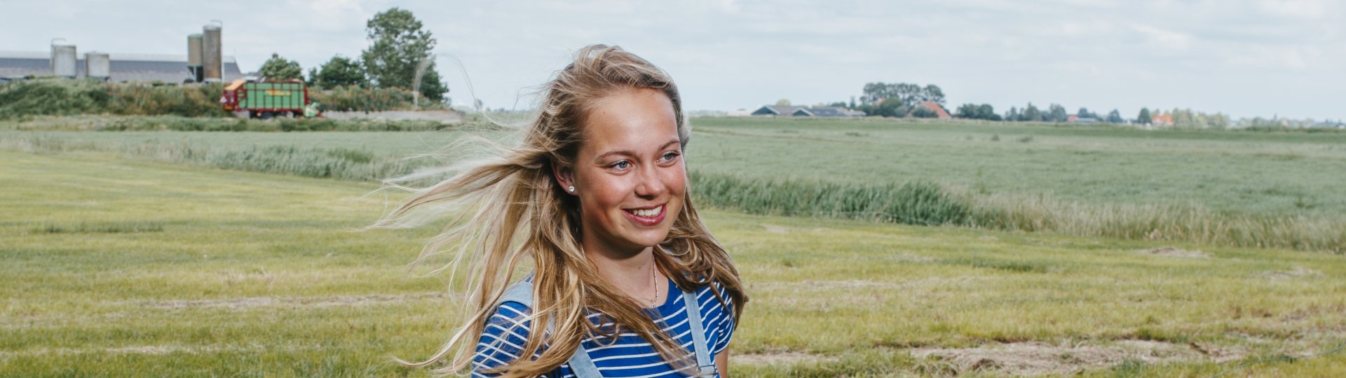 Een persoon in een weiland met een bord waarop staat 'mem sei: goed drinke mei dit waar!'