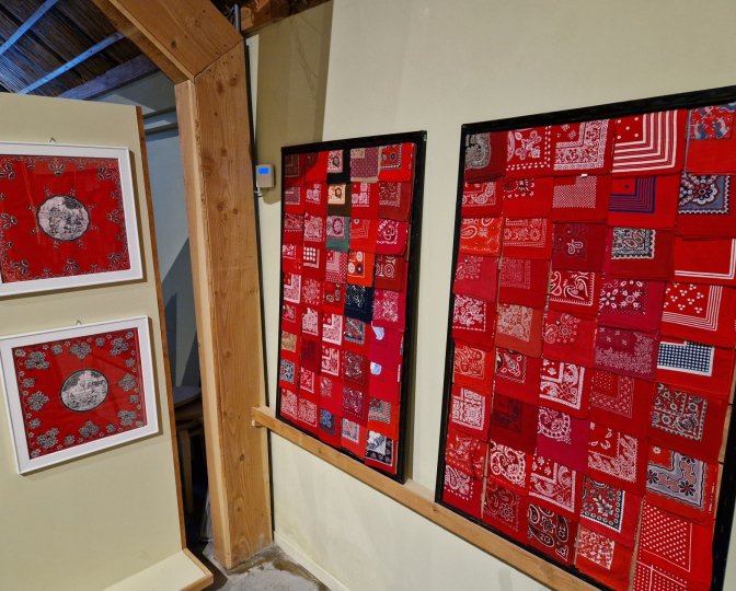 Een deel van de tijdelijke expositie van de rode boerenzakdoek in het Fries Landbouwmuseum. Links hangen twee zakdoeken in een lijst, aan de rechterkant zijn twee panelen te zien met een verzameling van zakdoeken erop.
