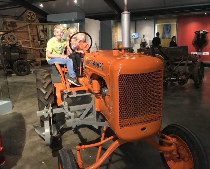 Twee kinderen zitten op de Allis-Chalmers trekker in het museum