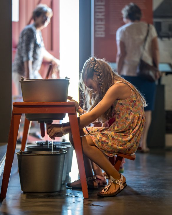 Kind zit op een melkkrukje in het museum de melkemmer te melken